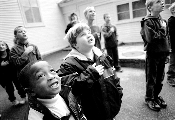 Six-year-old Stephon Willis, left, a first grade student at Wood School joins classmates in reciting the Pledge of Allegiance, Wednesday morning, prior to the start of school. Each morning, the 15 stu